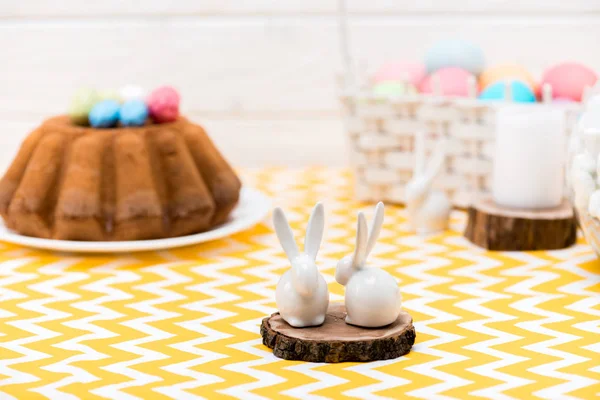 Керамические кролики, стоящие на столе с пасхальным хлебом и окрашенными яйцами — стоковое фото