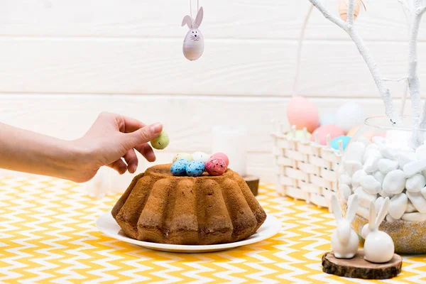 Cropped view of woman putting painted quail egg on easter cake in kitchen — Stock Photo