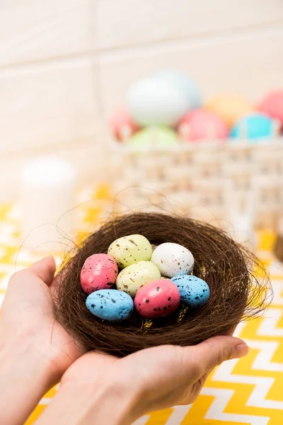 Partial view of woman holding nest with painted easter eggs — Stock Photo