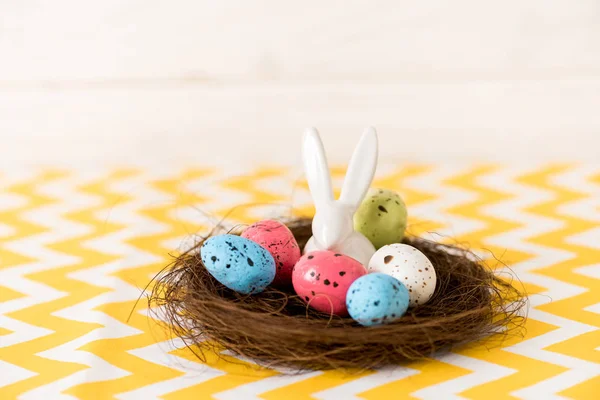 Nido con uova di Pasqua dipinte e coniglio in ceramica su superficie gialla — Stock Photo