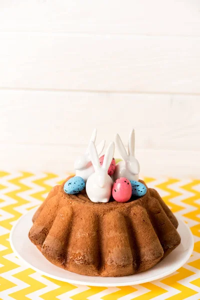 Pão de Páscoa com ovos de codorna pintados e coelhos cerâmicos na superfície amarela — Fotografia de Stock