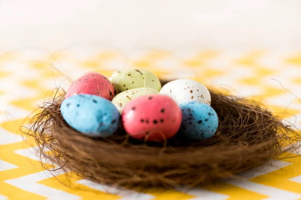 Nest with colorful painted easter eggs on yellow surface — Stock Photo