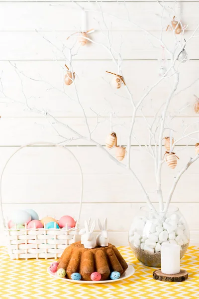 Easter bread and wicker basket with painted eggs on table on wooden — Stock Photo