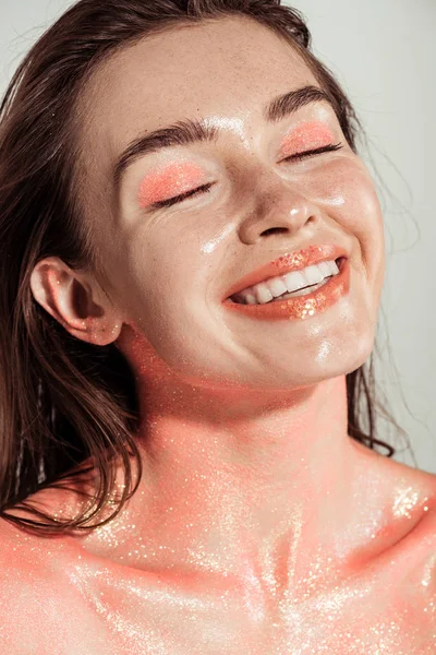 Beautiful smiling girl with coral glitter makeup and eyes closed posing isolated on grey — Stock Photo