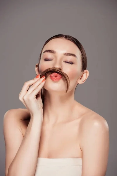 Beautiful girl pouting lips and holding hair as moustache isolated on grey — Stock Photo