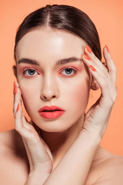 Beautiful stylish young woman looking at camera and touching face isolated on coral — Stock Photo