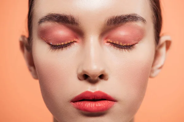 Bela jovem elegante com maquiagem brilho e olhos fechados isolados em coral — Fotografia de Stock