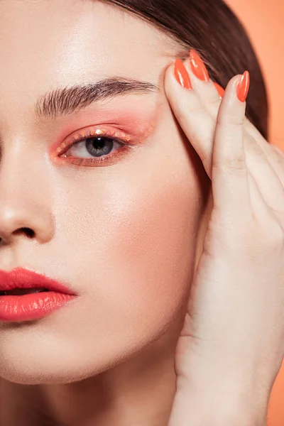 Hermosa mujer joven con estilo con maquillaje brillo mirando a la cámara aislada en coral - foto de stock