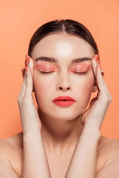 Beautiful trendy young woman with glitter makeup and eyes closed touching face isolated on coral — Stock Photo