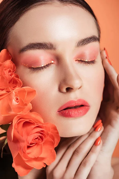 Bela menina elegante tocando rosto e posando com flores de rosas isoladas em coral — Fotografia de Stock