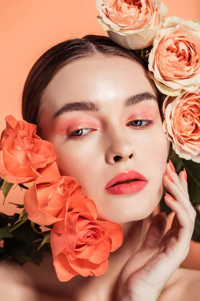 Bella ragazza elegante toccare il viso e in posa con fiori di rosa isolati su corallo — Foto stock