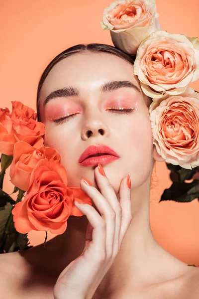 Belle fille élégante touchant le visage et posant avec des fleurs roses isolées sur le corail — Photo de stock