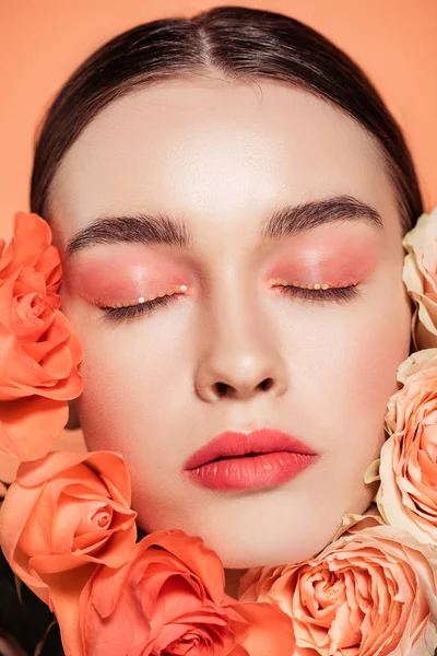 Beautiful trendy girl posing with rose flowers and eyes closed isolated on coral — Stock Photo