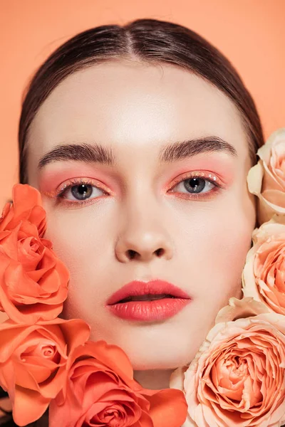 Atractiva chica con estilo mirando a la cámara y posando con flores de rosas aisladas en coral - foto de stock