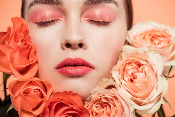 Belle fille à la mode posant avec des fleurs roses et les yeux fermés isolés sur le corail — Photo de stock