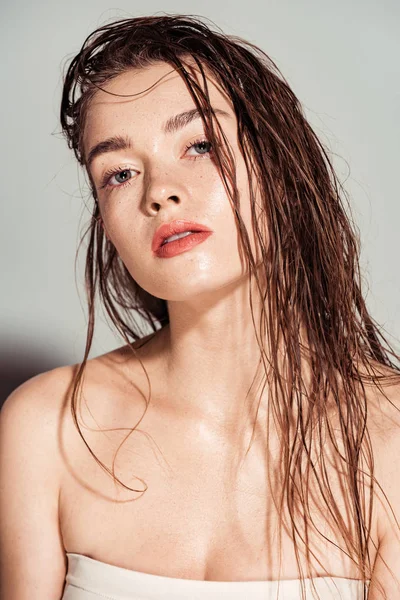 Bela jovem mulher com lábios de coral e cabelo molhado olhando para a câmera no fundo cinza — Fotografia de Stock