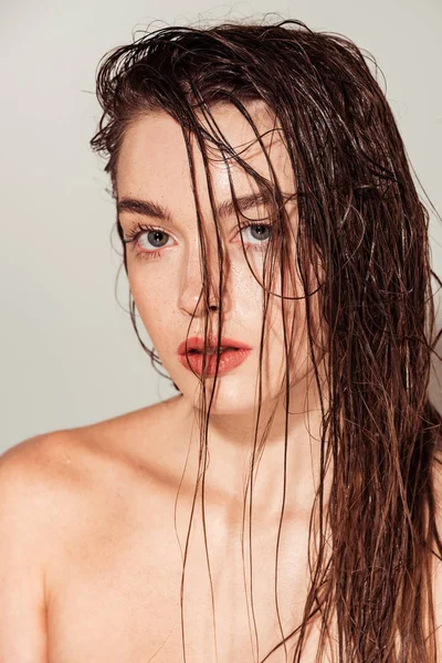 Beautiful nude young woman with coral lips and wet hair looking at camera while posing isolated on grey — Stock Photo
