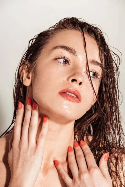 Menina atraente com lábios de coral e cabelo molhado olhando embora enquanto posando isolado no cinza — Fotografia de Stock