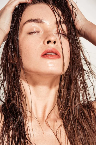Красива дівчина з кораловими губами, руками на голові і мокрим волоссям позує ізольовано на сірому — стокове фото