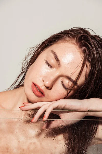 Hermosa joven con labios de coral tocando la cara mientras posa cerca de acuario aislado en gris - foto de stock