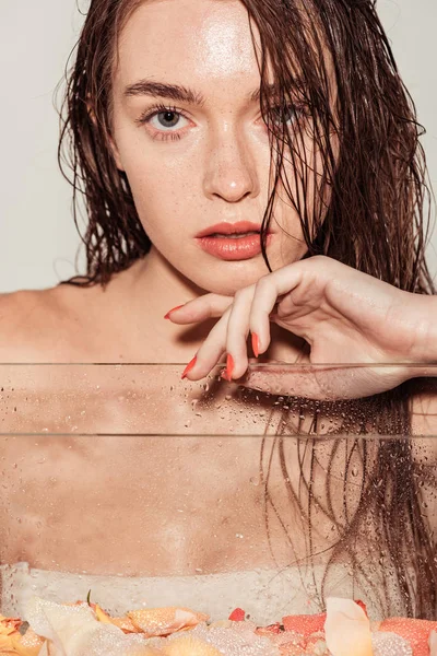 Belle jeune femme avec des lèvres de corail regardant caméra tout en posant près de l'aquarium isolé sur gris — Photo de stock