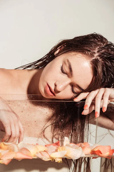 Menina bonita com lábios de coral e olhos fechados posando perto do aquário com pétalas de rosa isoladas em cinza — Fotografia de Stock