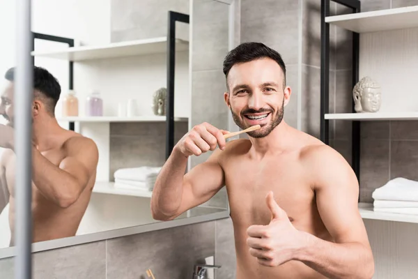 Веселий чоловік показує великий палець, тримаючи зубну щітку у ванній — стокове фото