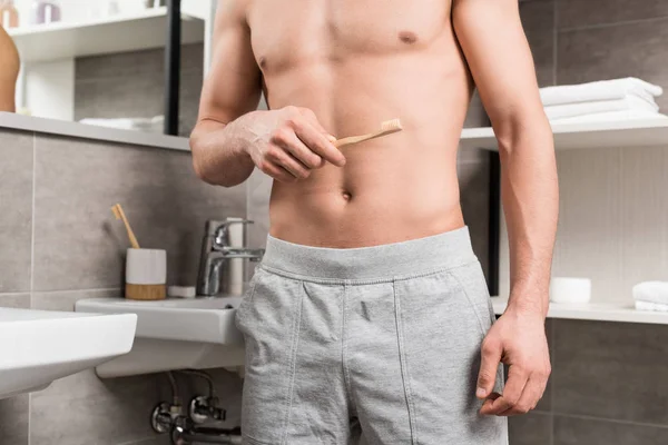 Vista recortada del hombre sosteniendo el cepillo de dientes mientras está de pie en el baño - foto de stock