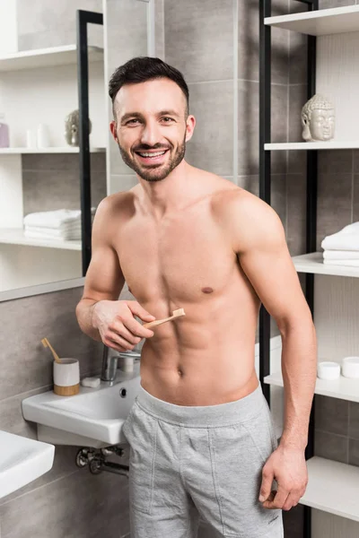 Hombre alegre sosteniendo el cepillo de dientes mientras está de pie en el baño - foto de stock