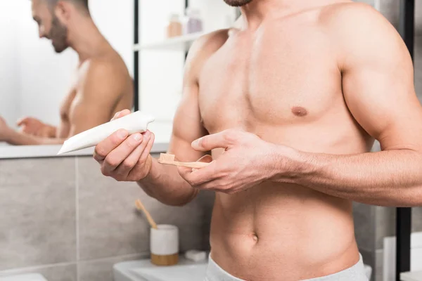 Vista recortada del hombre sin camisa sosteniendo pasta de dientes y cepillo de dientes en el baño - foto de stock