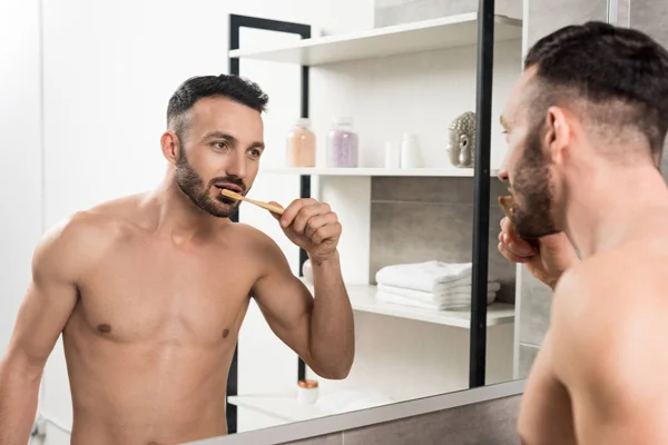 Barbuto uomo senza maglietta lavarsi i denti mentre si guarda specchio in bagno — Foto stock