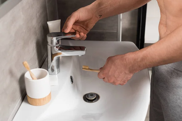 Vista recortada del hombre sosteniendo cepillo de dientes cerca del lavabo en el baño - foto de stock