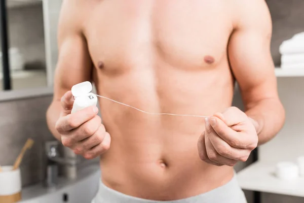 Cropped view of shirtless man holding dental floss while standing in bathroom — Stock Photo