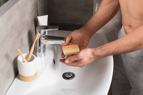 Vista recortada del hombre que sostiene el jabón cerca del lavabo mientras está de pie en el baño - foto de stock