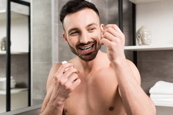 Bearded man using dental floss while standing in bathroom — Stock Photo