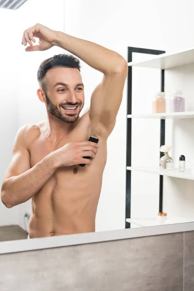 Happy shirtless man shaving armpit while looking at mirror in bathroom — Stock Photo