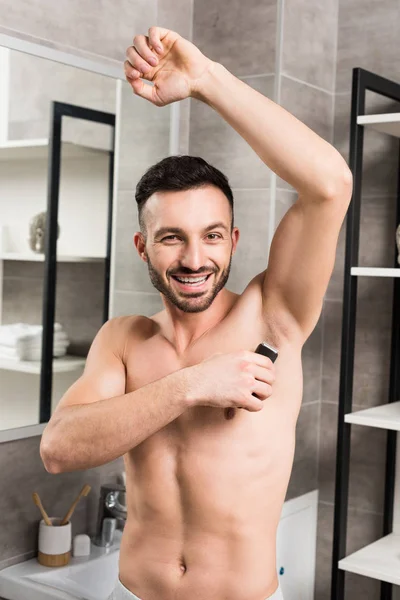 Весёлый мужчина без рубашки бреет подмышки в ванной — стоковое фото