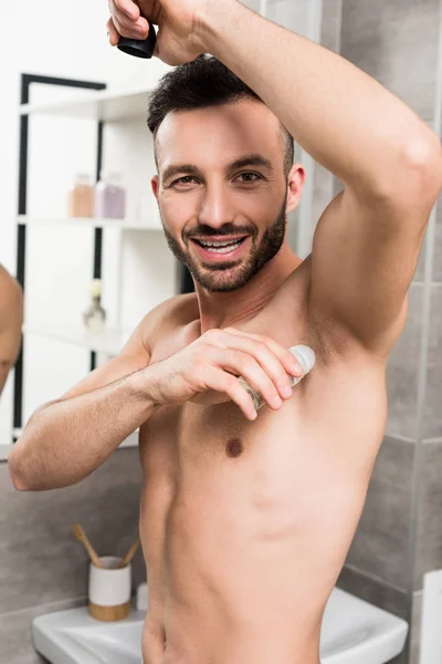 Glücklicher, hemdloser Mann, der im Badezimmer Deo aufträgt — Stockfoto