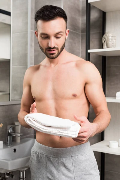 Bonito sem camisa homem segurando branco toalha no banheiro — Fotografia de Stock