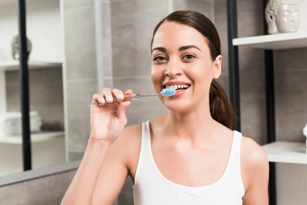 Foco seletivo de mulher morena feliz escovando dentes no banheiro — Fotografia de Stock