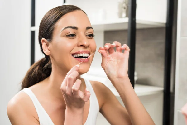 Mulher morena alegre usando fio dental no banheiro — Fotografia de Stock