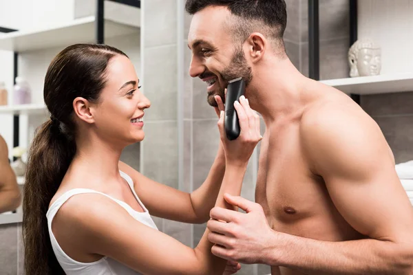 Mujer atractiva afeitándose la cara de novio sin camisa guapo en el baño - foto de stock