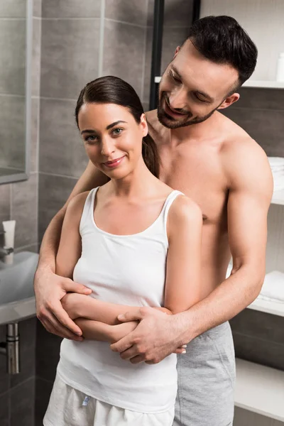 Fröhlicher bärtiger Mann umarmt attraktive Freundin im Badezimmer — Stockfoto