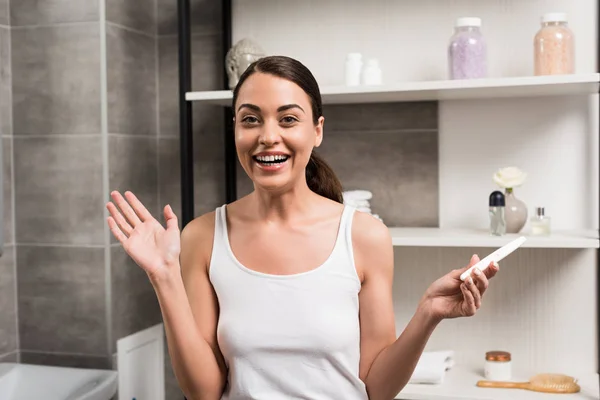 Excitée femme brune tenant test de grossesse dans la salle de bain — Photo de stock