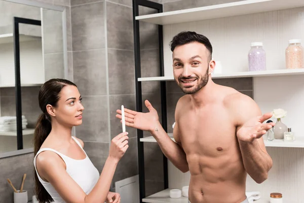 Donna che tiene il test di gravidanza vicino a camicia fidanzato mostrando gesto scrollata di spalle — Foto stock