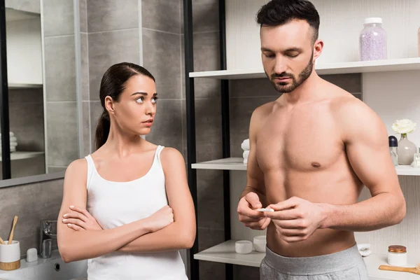 Worried woman standing with crossed arms and looking at boyfriend holding pregnancy test — Stock Photo