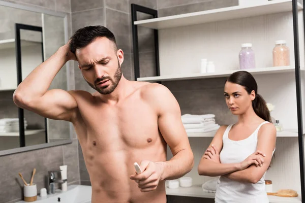 Селективное внимание мужчины без рубашки, держащего тест на беременность рядом с девушкой, стоящей со скрещенными руками — стоковое фото