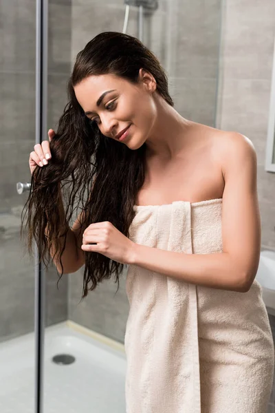 Веселая женщина касается мокрых волос, стоя в ванной — стоковое фото