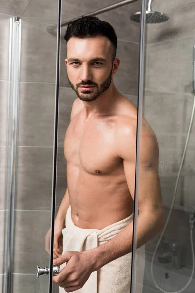 Musclé bel homme debout dans la cabine de douche dans la salle de bain moderne — Photo de stock