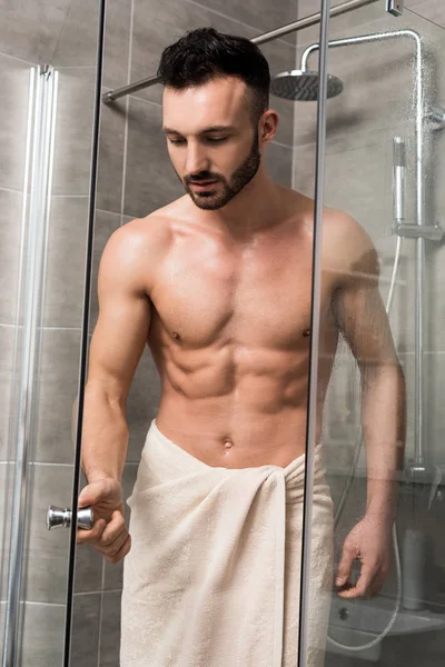 Musclé bel homme debout dans la cabine de douche dans la salle de bain moderne — Photo de stock